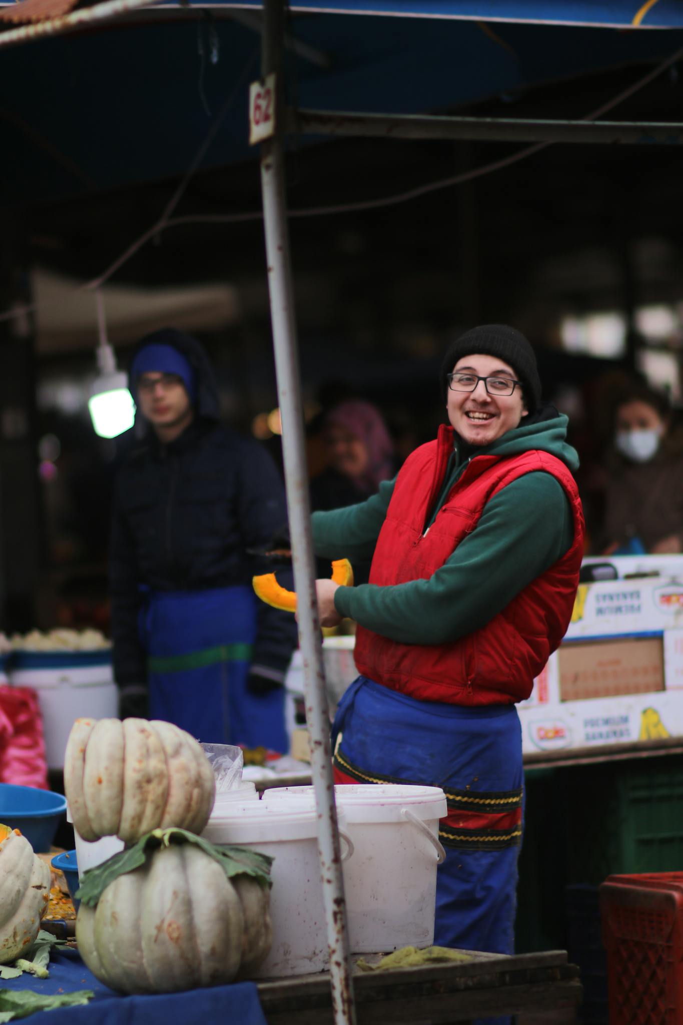 A cheerful vendor displaying pumpkins at a bustling outdoor market.