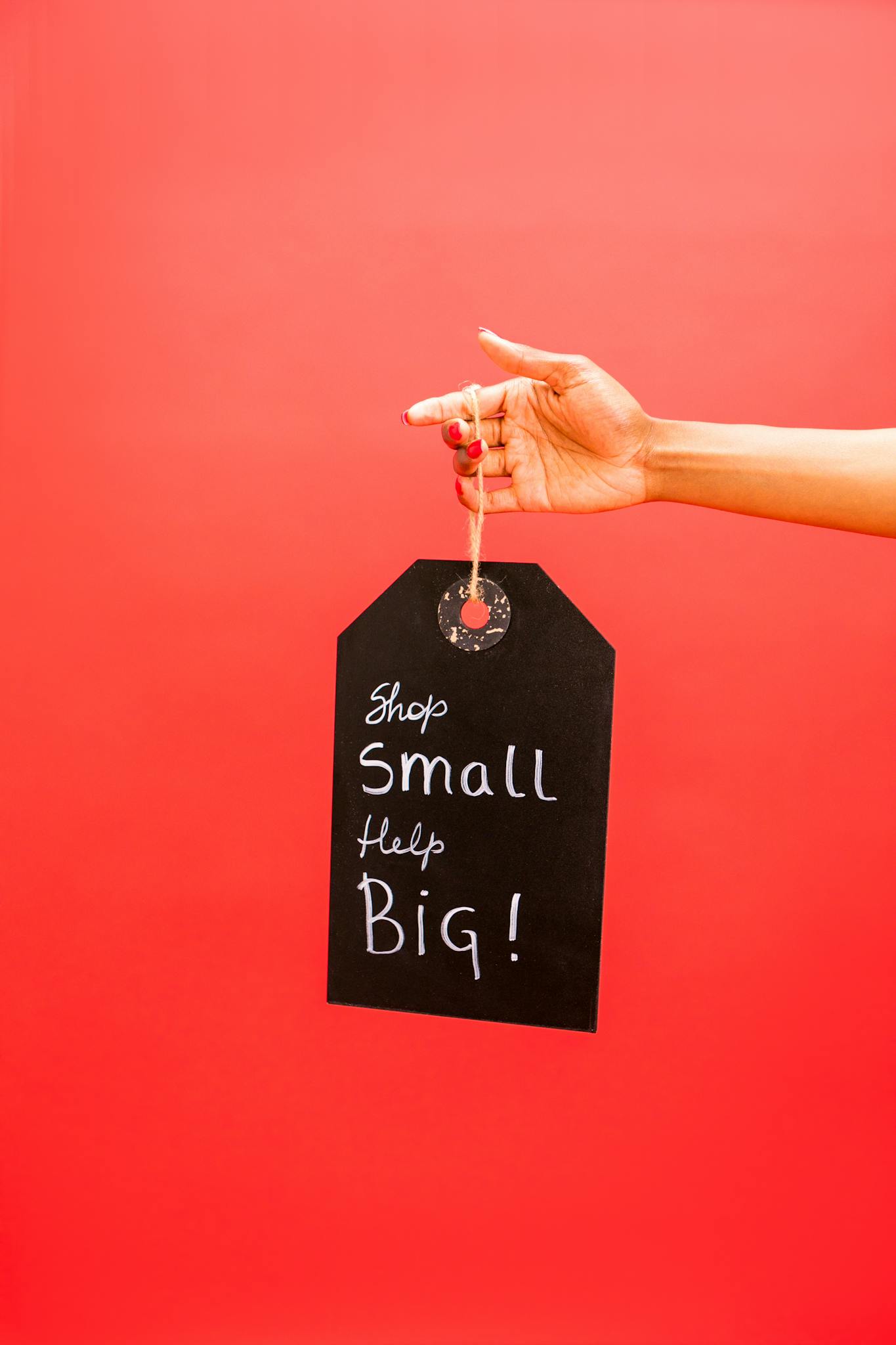 A hand holding a sign that reads 'Shop Small Help Big' against a red background.